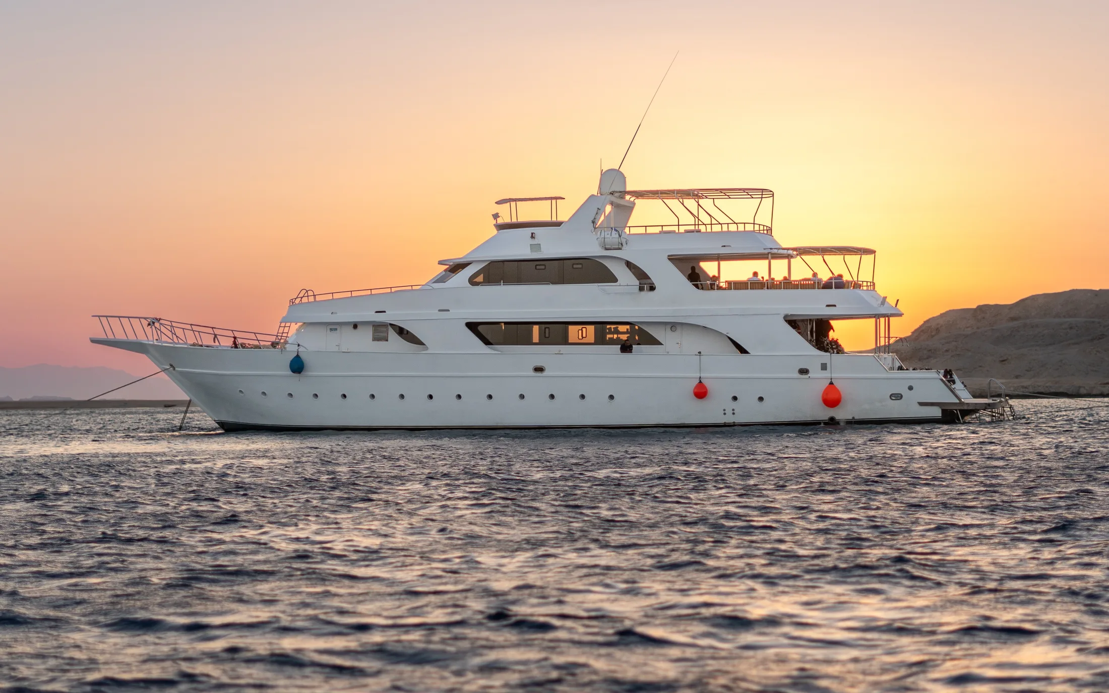 The liveaboard in profile at sunset, a headland behind